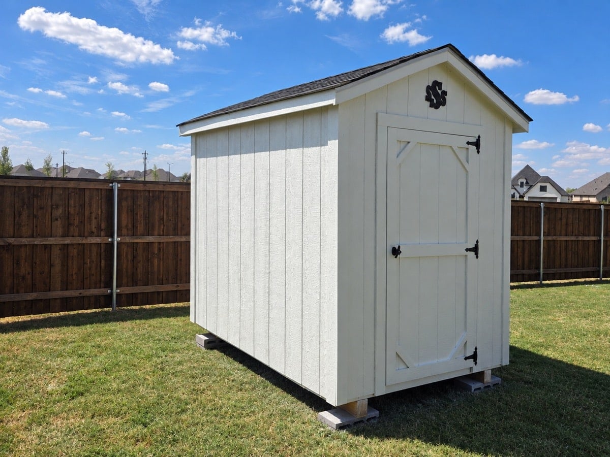 White shed with a dark roof and single door in a fenced backyard